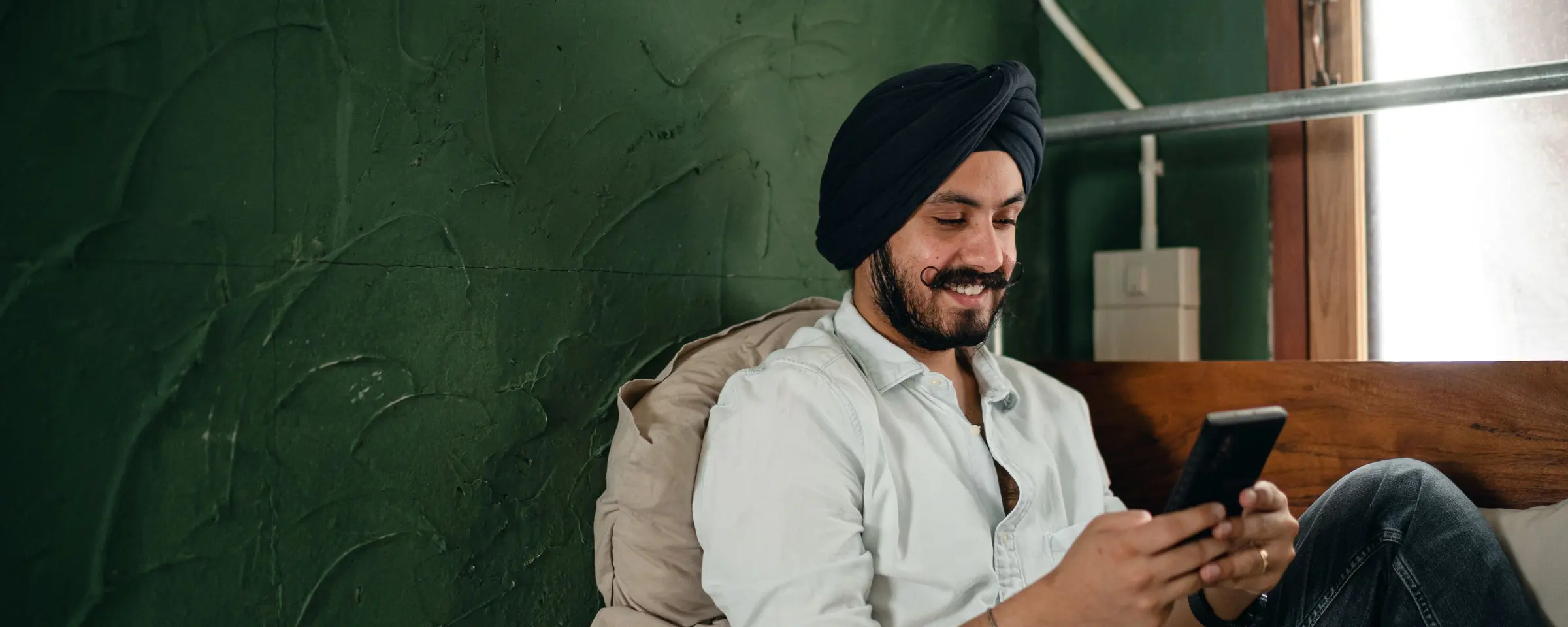A smiling man sitting at home, sending money from his phone