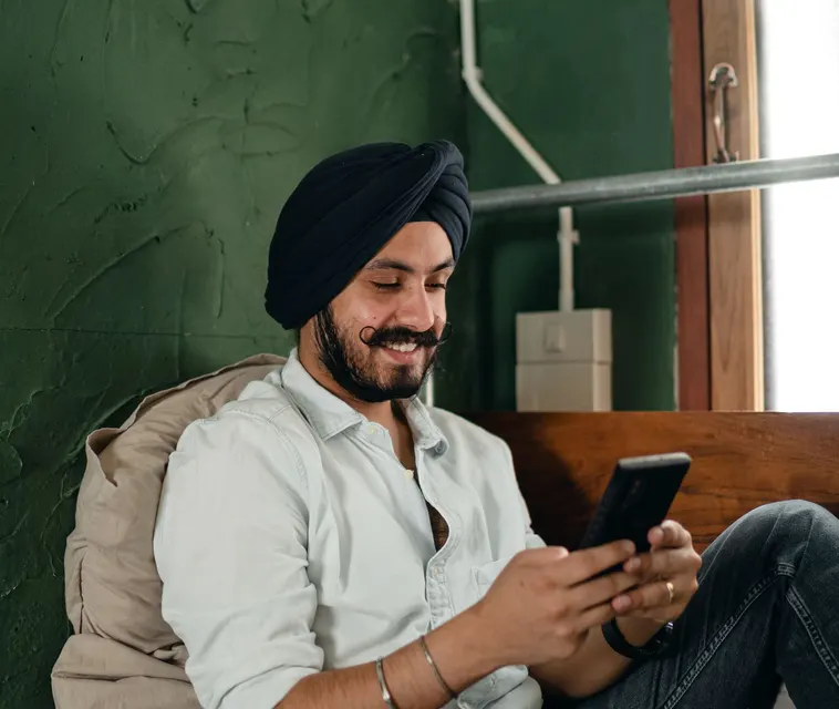 A smiling man sitting at home, sending money from his phone