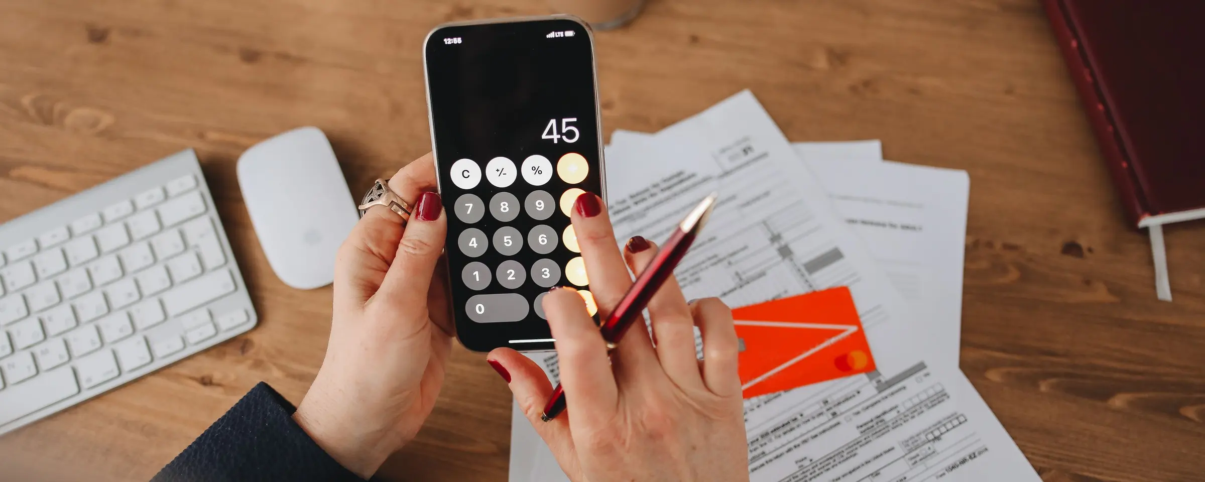 Hands using a phone calculator over a stack of bills
