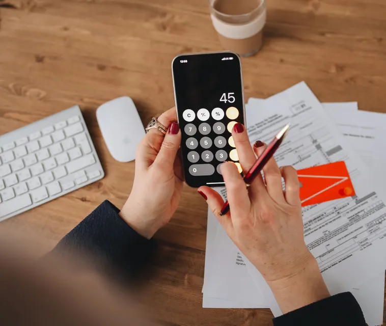 Hands using a phone calculator over a stack of bills