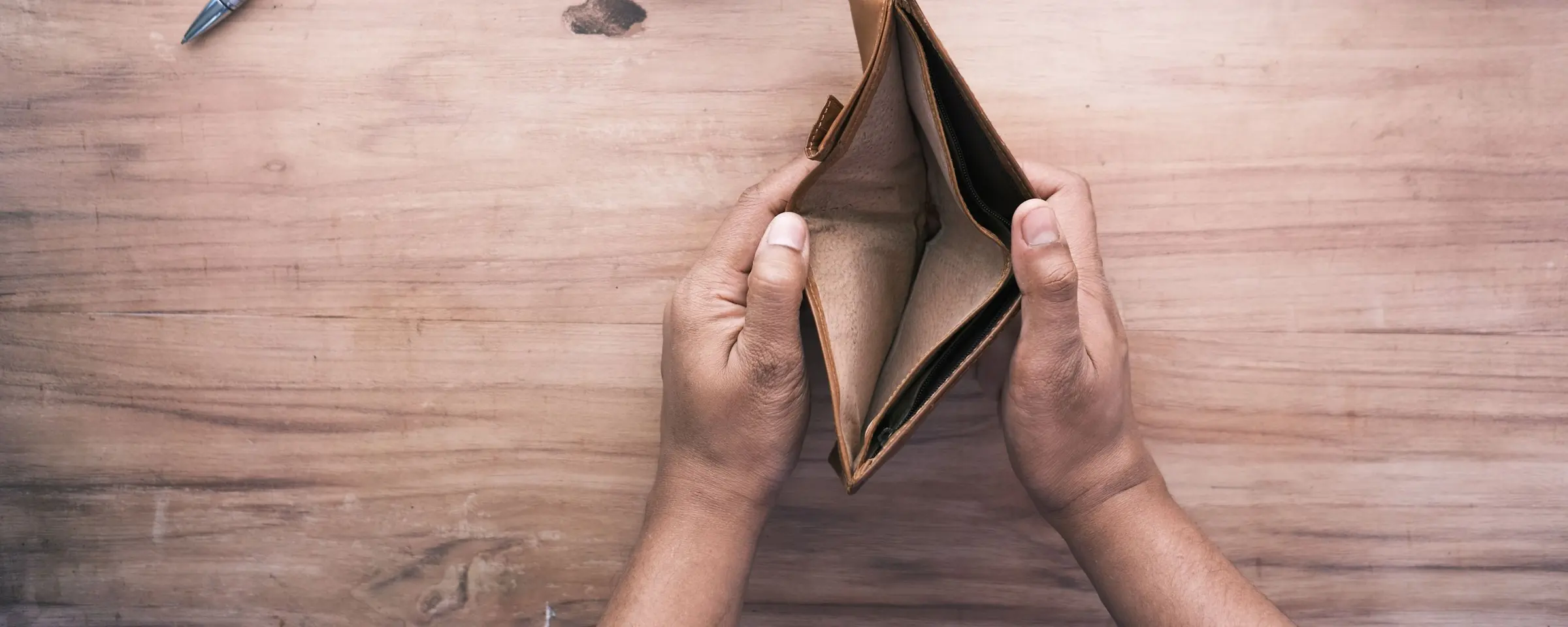 Hands holding an open, empty wallet over a desk
