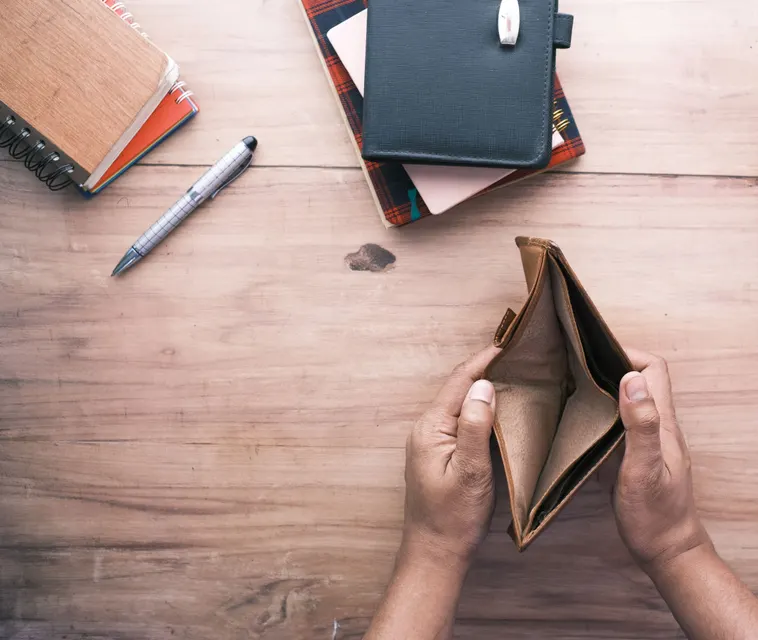 Hands holding an open, empty wallet over a desk