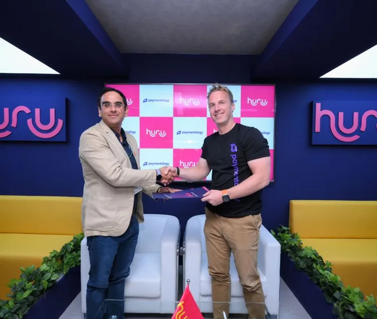 Huru and Paymentology representatives shaking hands at their partnership signing, between two Huru logos